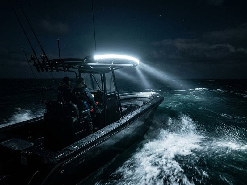 Rampe LED incurvée allumée sur bateau de pêche en navigation nocturne, faisceau panoramique puissant éclairant la mer agitée