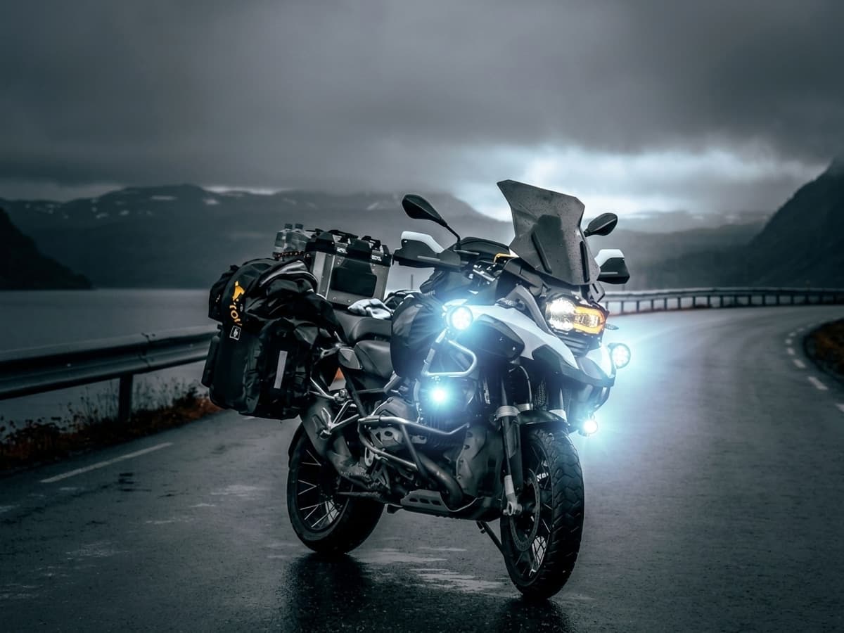 Phare LED additionnel allumé sur moto trail enduro de nuit en forêt, faisceau puissant éclairant un sentier boueux