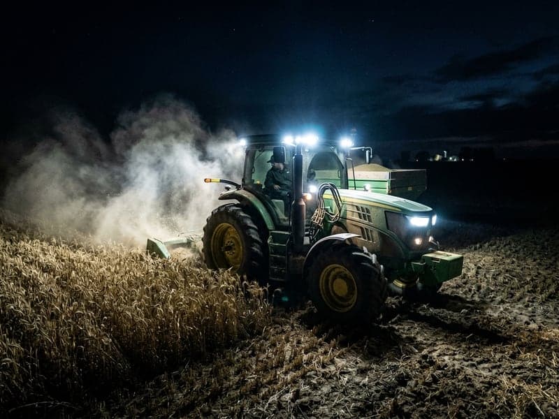 Tracteur agricole travaillant de nuit avec phares LED puissants éclairant un champ de maïs poussiéreux